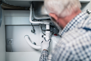 Senior man plumber working with plumbing tools on the kitchen. Renovation.