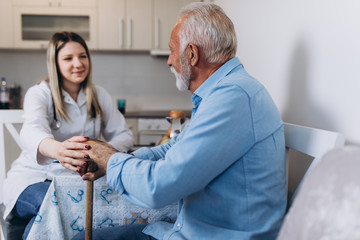 Young positive caregiver taking care of senior man in nursing home