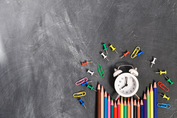 Alarm clock, colored pencils and stationery on black school Board background