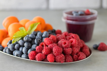 Fruit and berry smoothies. Fresh apricots, raspberries and blueberries on an oval metal plate. Gray background.