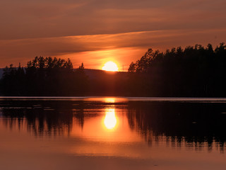 Sunset in Swedish coutry side landscape. The lake is mirroring the forest and sun.