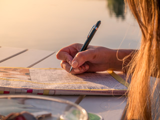 Woman is solving a crossword puzzle paper. Calm summer holiday activity.