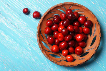 Red sweet cherry in a clay plate on a turquoise wooden table