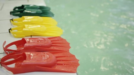 Diving fins in three different colors at the edge of the pool. Green yellow red color. Fins made of rubber and plasmass for swimming on a background of water.