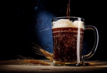 close up of beer in glass with barley on on dark background .