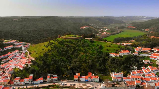 Aerial Panoramic Zoom Out Castle of Aljezur. Drone Flyng from Medieval fortress on hill over Algarve touristic city. Countryside green lush vegetation, fields and rural landscape with houses.