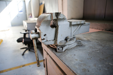 Shallow depth of field image with a rusty and dirty heavy iron vice on a workbench inside a workshop with no people around