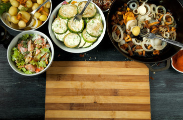 Vegetables on the background. Fried zucchini sauce in a plate. Young boiled potatoes with dill in a bowl. Fried chanterelle mushrooms with golden onions in a frying pan. copy space