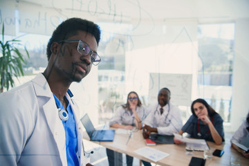 Fototapeta premium African professor at medical conference in modern clinic teaches his students. Doctor writing on board some formulas for interns in conference room at hospital at sunrise.