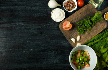 Salad with vegetables. View from above. Fresh salad in a plate on a dark background. Garlic, tomato, cucumber, dill and onion in a dish of dark surface. Copy space.