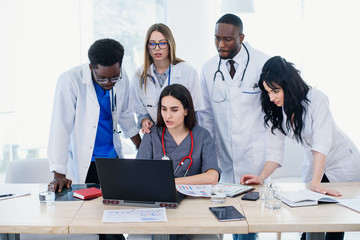 Group of multi national doctors using laptop for discussing analysis in the conference room. Side...