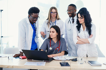 Fototapeta premium Group of multi national doctors using laptop for discussing analysis in the conference room. Side view.