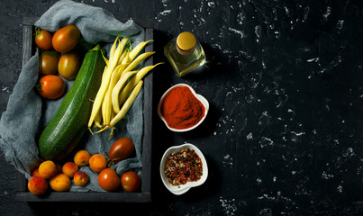 Vegetables on a dark background. Spices, oil, zucchini, asparagus, beans, tomato, peaches on a dark textured surface. View from above. copy space.