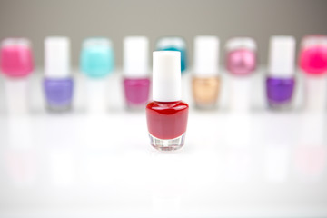 View on a shiny white desk full of small glass and plastic bottles with assorted nail polish and lacquer with focus on one red nail polish.