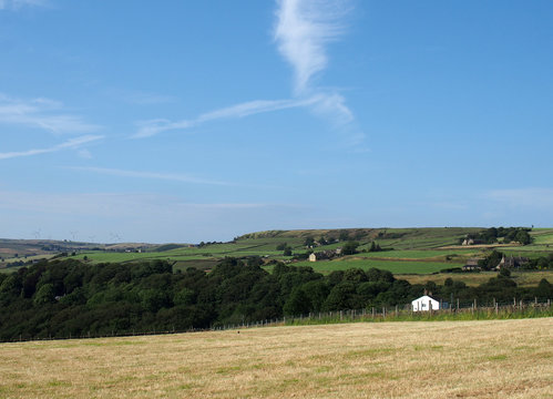 a cut summer hay meadow surrounded by green fields and farmhouses with a blue sunlit sky above the village of luddenden in calderdale west yorkshire