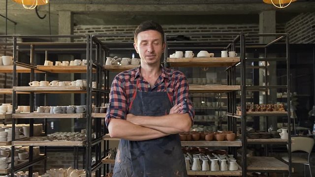 Attractive male potter crossing hands and looking to camera in the pottery.