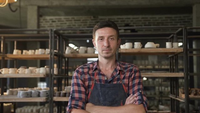 Happy male potter crossing hands and looking to camera in the pottery.