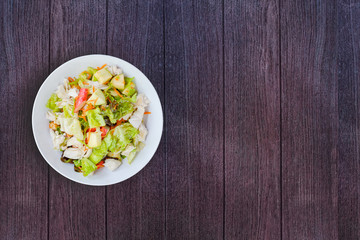 Top view. Boiled chicken salad with apple,  Crab sticks, carrot sliced, lettuce in white bowl on wooden background. Healthy food to high fiber, vitamins and low carbohydrate, fat. Copy space for your 
