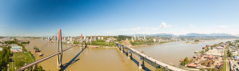 Obraz premium Aerial panoramic view of Pattullo Bridge and Skytrain Bridge over the Fraser River. Taken in Surrey, Greater Vancouver, British Columbia, Canada.