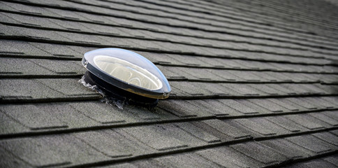 Dome shaped solar tube skylight on asphalt shingle roof 