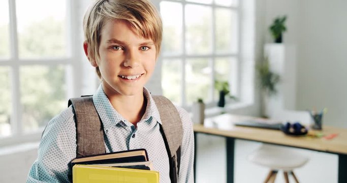 Smiling schoolboy with backpack holding textbooks and smiling to camera, back to school