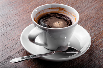 white porcelain cup of coffee close-up with spoon and saucer  on  wooden background