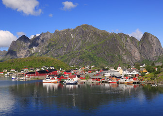 Traditional red colorful Norwegian fishing houses in Reine with mountains on the background, ...