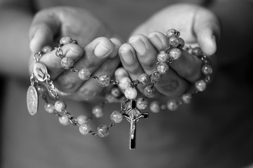 Rosary in hand in black and white. Young junior lady holding rosary with open hand with Jesus...