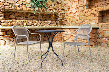 Fototapeta na wymiar Table and chairs on pebble ground outside house with brick wall in background
