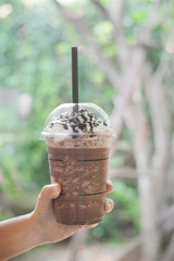 Hand holding of whip cream on delicious and cold white chocolate mocha drink in glass with natural background.