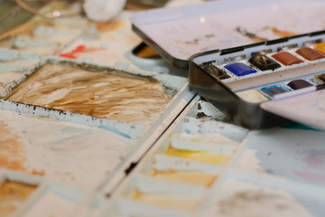 Selective focus of tools for painting on the wooden table. Brushes, paper and paints on the table. Painter's workpace.