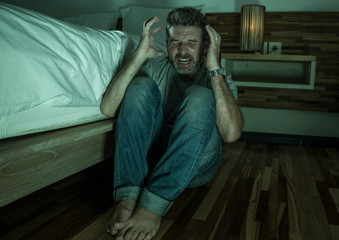 dramatic home portrait of young desperate and depressed lonely man sitting on bedroom floor crying...