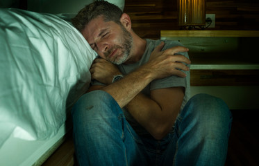 dramatic home portrait of young desperate and depressed lonely man sitting on bedroom floor crying...