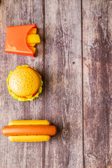 Plastic burger, salad, tomato, frying potatoes with hot dog on a wooden background. Vertical orientation. Children's toy. The concept of harmful artificial food. Plastic Not organic. Not healthy.