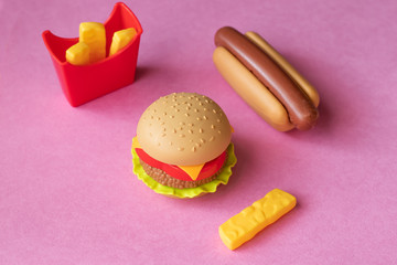 Plastic burger, salad, tomato, frying potatoes with a hot dog on a pink background. Horizontal orientation. Children's toy. The concept of harmful artificial food. Plastic Not organic. Not healthy.