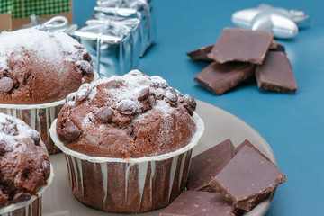 Three chocolate muffins lie on a plate against the background of a turquoise-colored table. Celebration. Christmas and New Year.