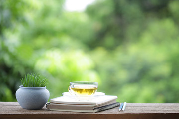 Greentea in transpalent glass and diary notebook with tree plant pot on wooden table