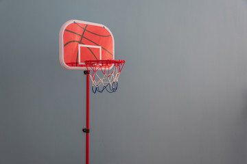 A red toy basketball stand for children's games stands in front of a gray background wall
