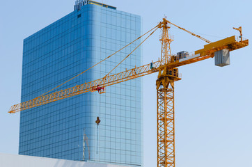 Construction crane on the background of an office building with a mirror surface