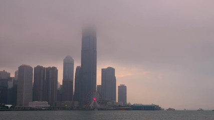 Time lapse of Hong Kong cityscape with sun light in the hard mist at the harbor in the raining day
