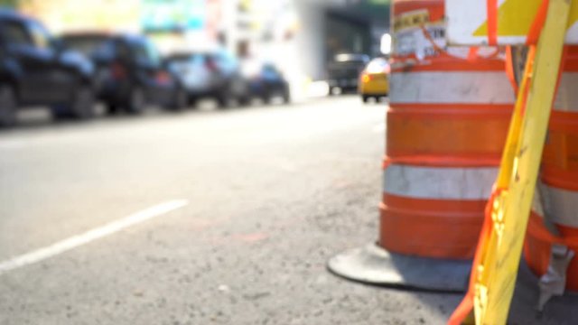 New York City Streets defocused behind orange roadwork cones and warning sign, yellow taxi cab and bike commuters in the background