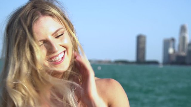 Beautiful Caucasian blonde female with green/blue eyes looks directly into the camera seductively then laughs happily as the wind blows her hair. the Chicago rivers flows towards the tourist city