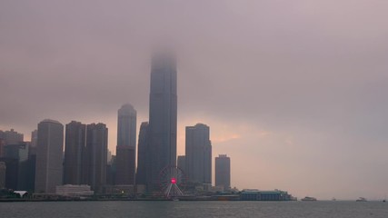 Time lapse of Hong Kong cityscape with sun light in the hard mist at the harbor in the raining day