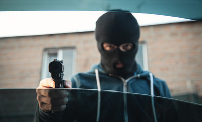 Car theft in black mask with a pistol.