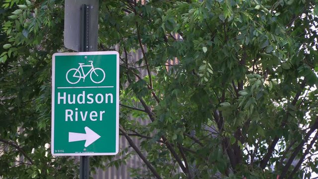 Hudson River street sign showing bike lane and path for New York City visitors and commuters, subtle NYC video background