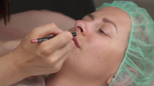 Permanent tattoo . Permanent lips make-up work performed in a beauty salon. Woman having lip drawn and tinted with pencil, preparing for semi-permanent makeup.