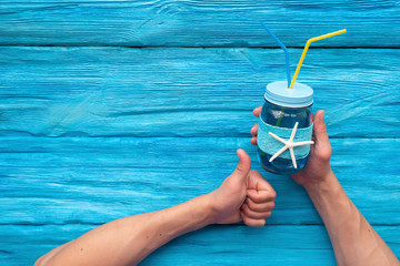Sea cocktail in a transparent glass jar in male hand over blue wooden background with copy space.