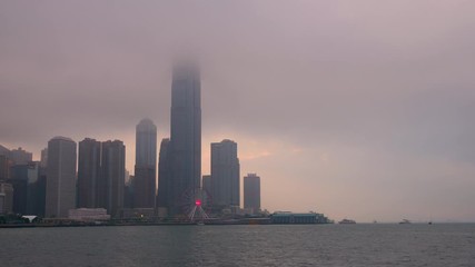 Time lapse of Hong Kong cityscape with sun light in the hard mist at the harbor in the raining day