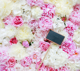 Blank blackboard label lying on flower background with peonies, roses and hortensias.