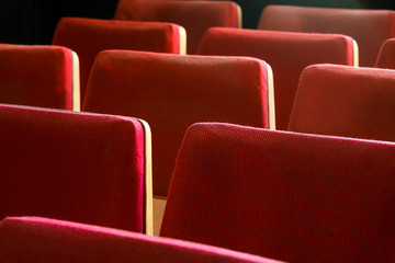 Old tired cinema seats covered with worn red velvet. Empty red chairs in theatre. Red theater seats